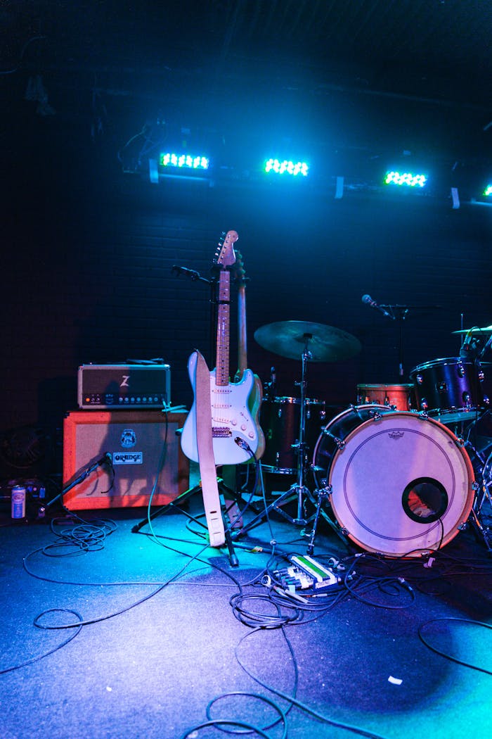 about-us-01 Electric guitar and drum set on an illuminated live music stage, ready for performance.