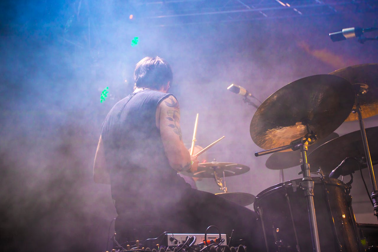 services-02 Energetic drummer performing live on stage with colorful smoke and lighting effects.
