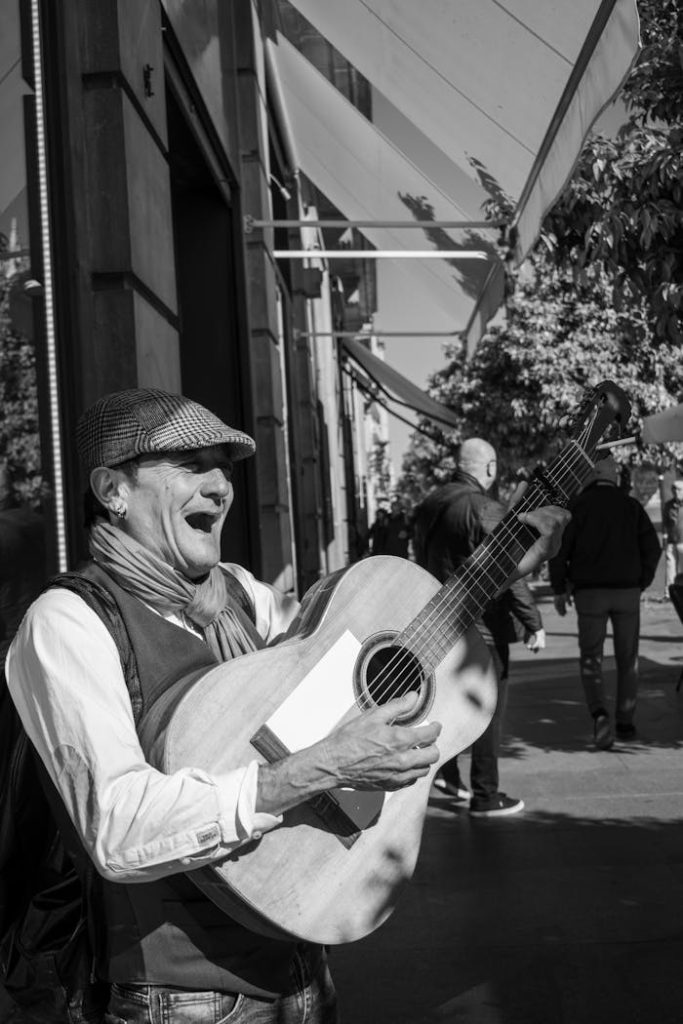 Black and white photo of a man joyfully playing an acoustic guitar on a Seville street.